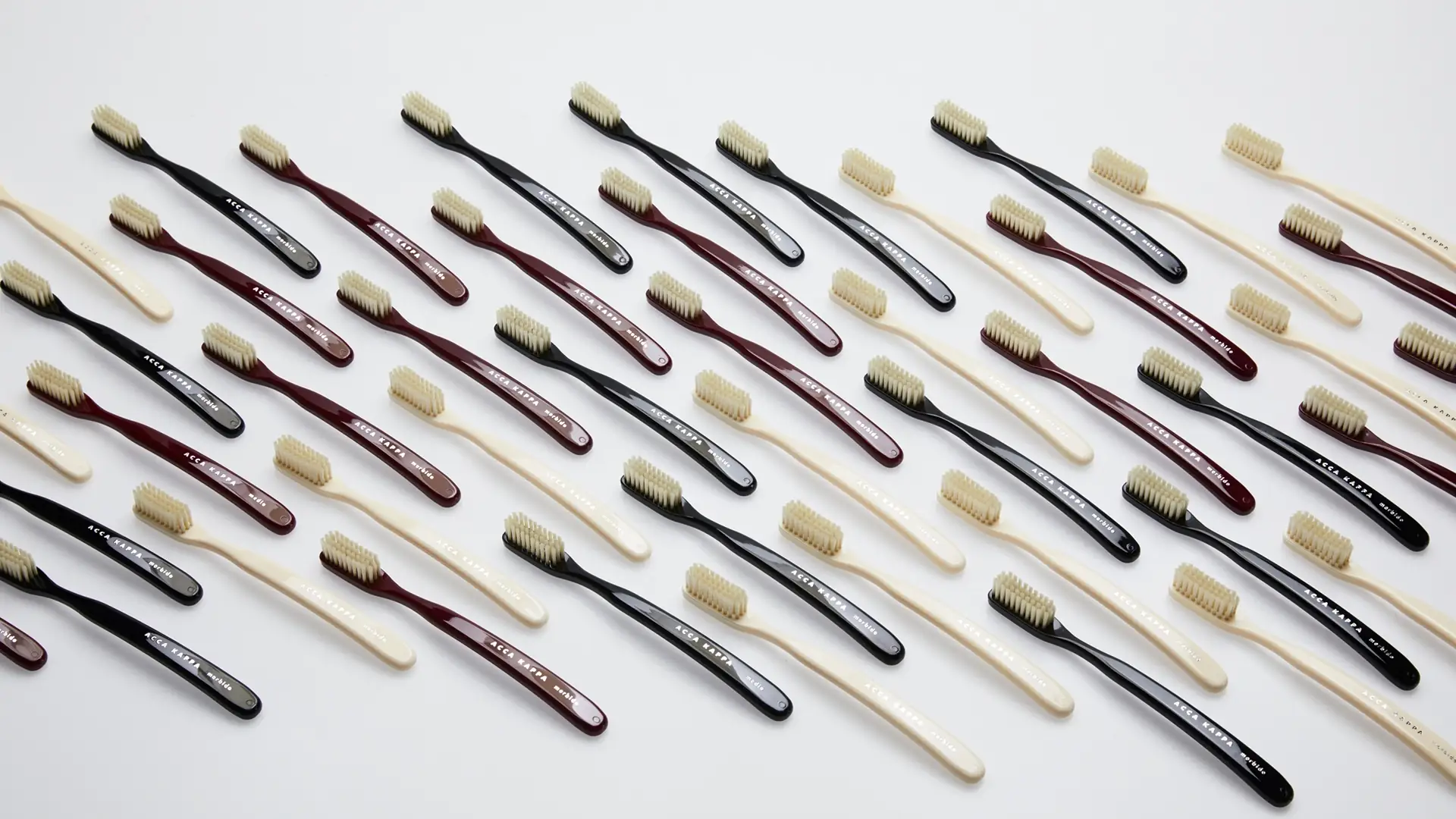 Multiple toothbrushes in black, maroon, and cream colors arranged diagonally on a white surface, bristle heads facing upward.