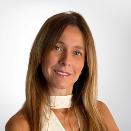Portrait of a smiling woman with long brown hair, wearing a white sleeveless top, against a neutral background.