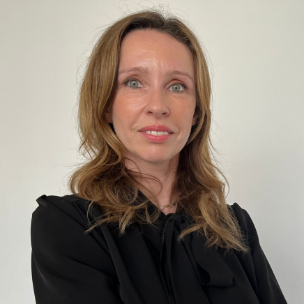 Head-and-shoulders portrait of a woman with light brown hair wearing a black blouse, looking at the camera with a slight smile against a plain light background.