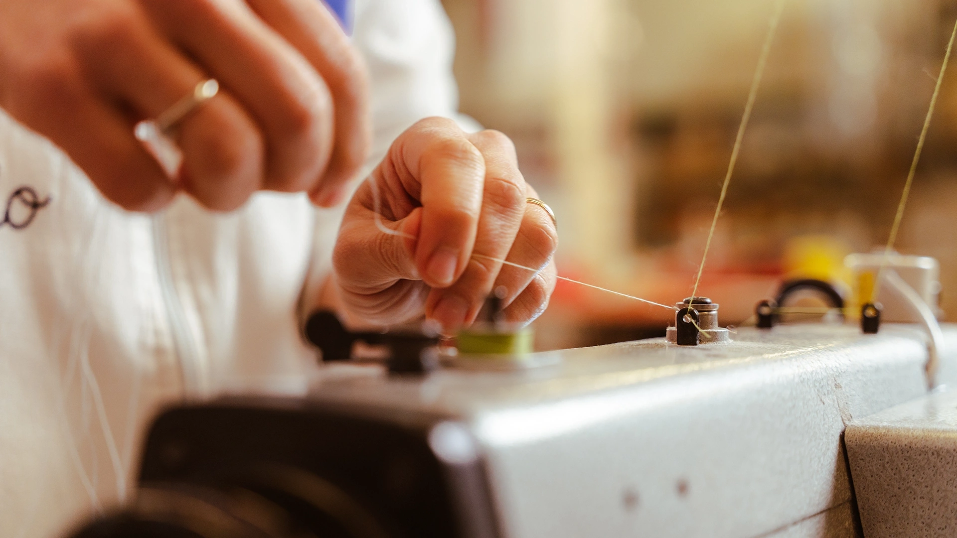 Close-up of hands threading a sewing machine, with thread and spool visible on the machine surface