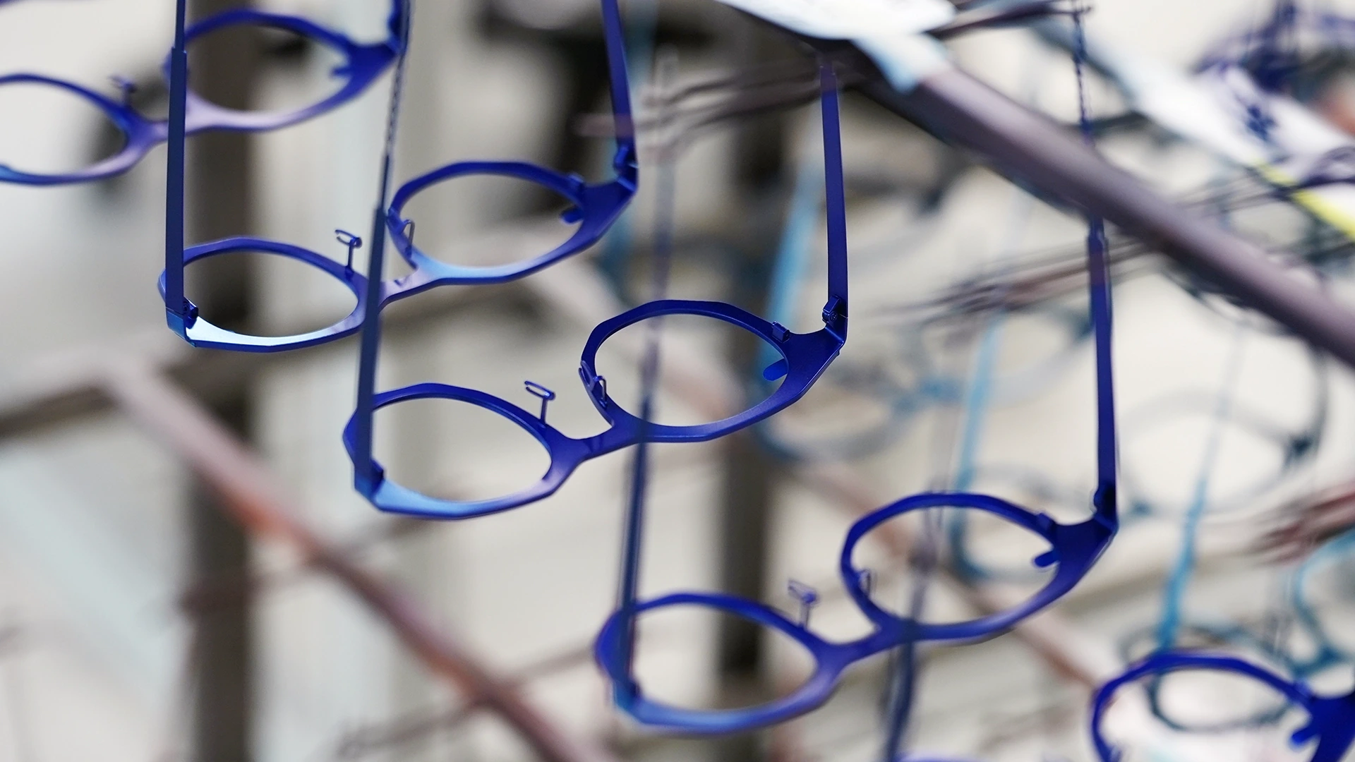 Blue circular eyeglass frames hanging on wires in a blurred background.