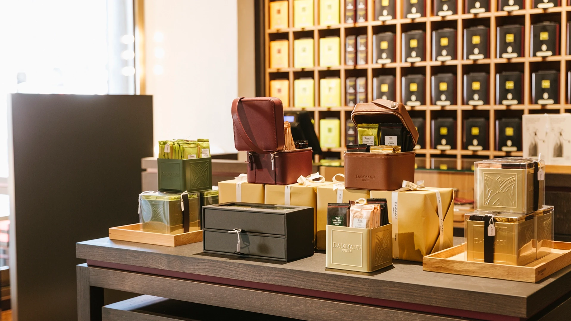 Luxurious gift sets including brown leather cases and gold boxes arranged on a wooden table in a store, with shelves of boxed products behind.
