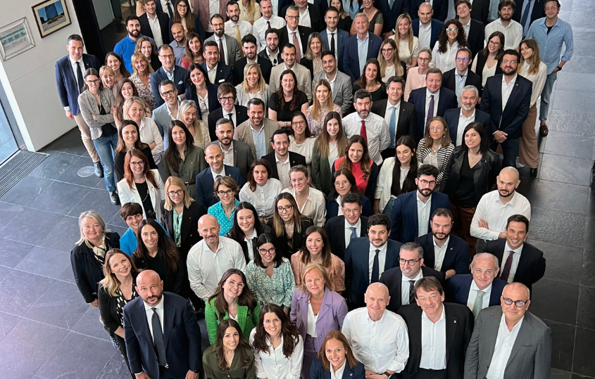 Large diverse group of professionals posing for a group photo in a modern office lobby. (informative)