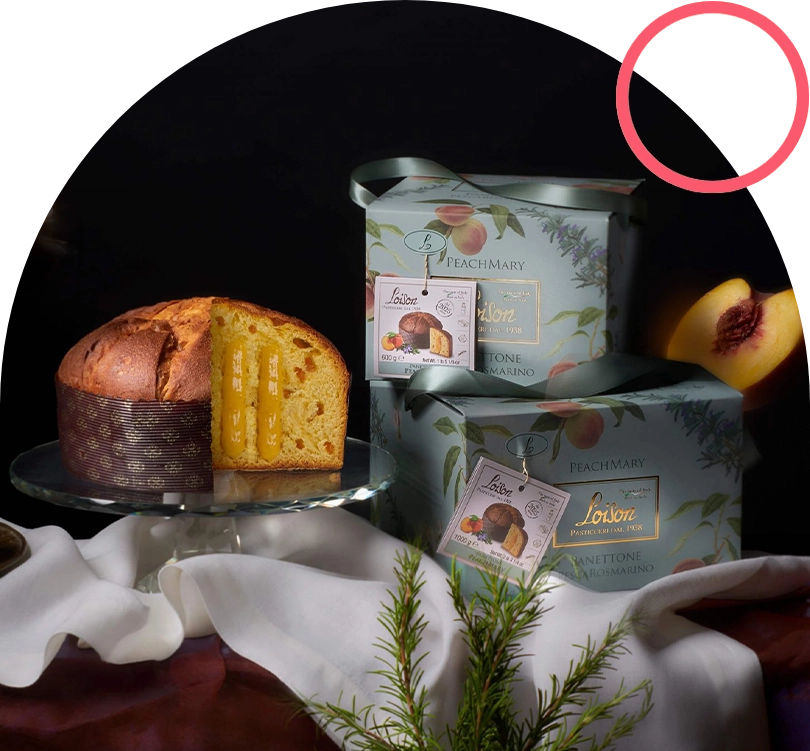Cake with peach filling on a glass stand beside pastel peach-themed gift boxes and peaches under a dark background.