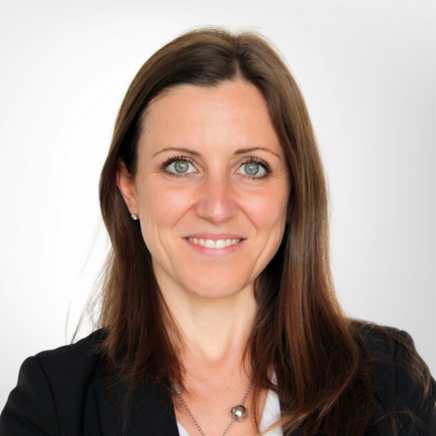 Professional headshot of a smiling woman with shoulder-length brown hair, wearing a black blazer and white blouse against a light background.