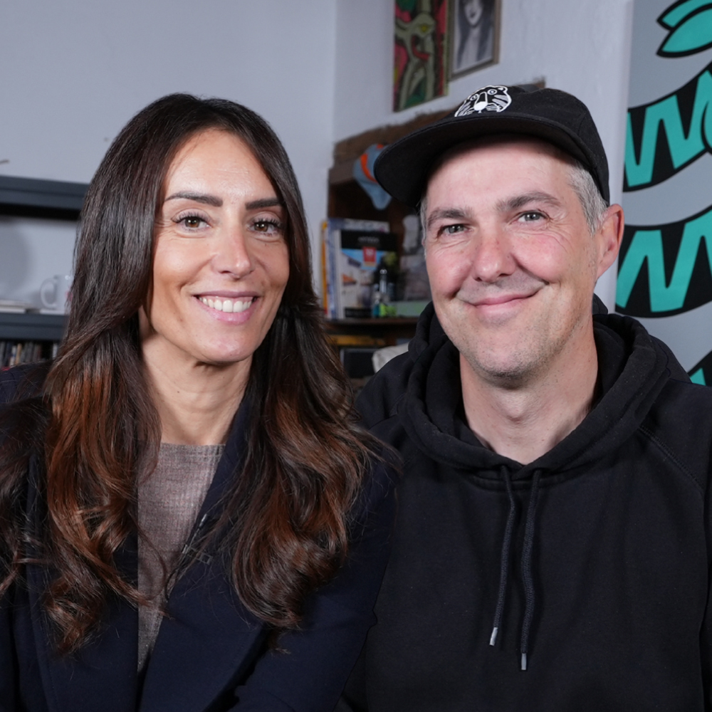 Two people smiling at the camera in an indoor setting.
