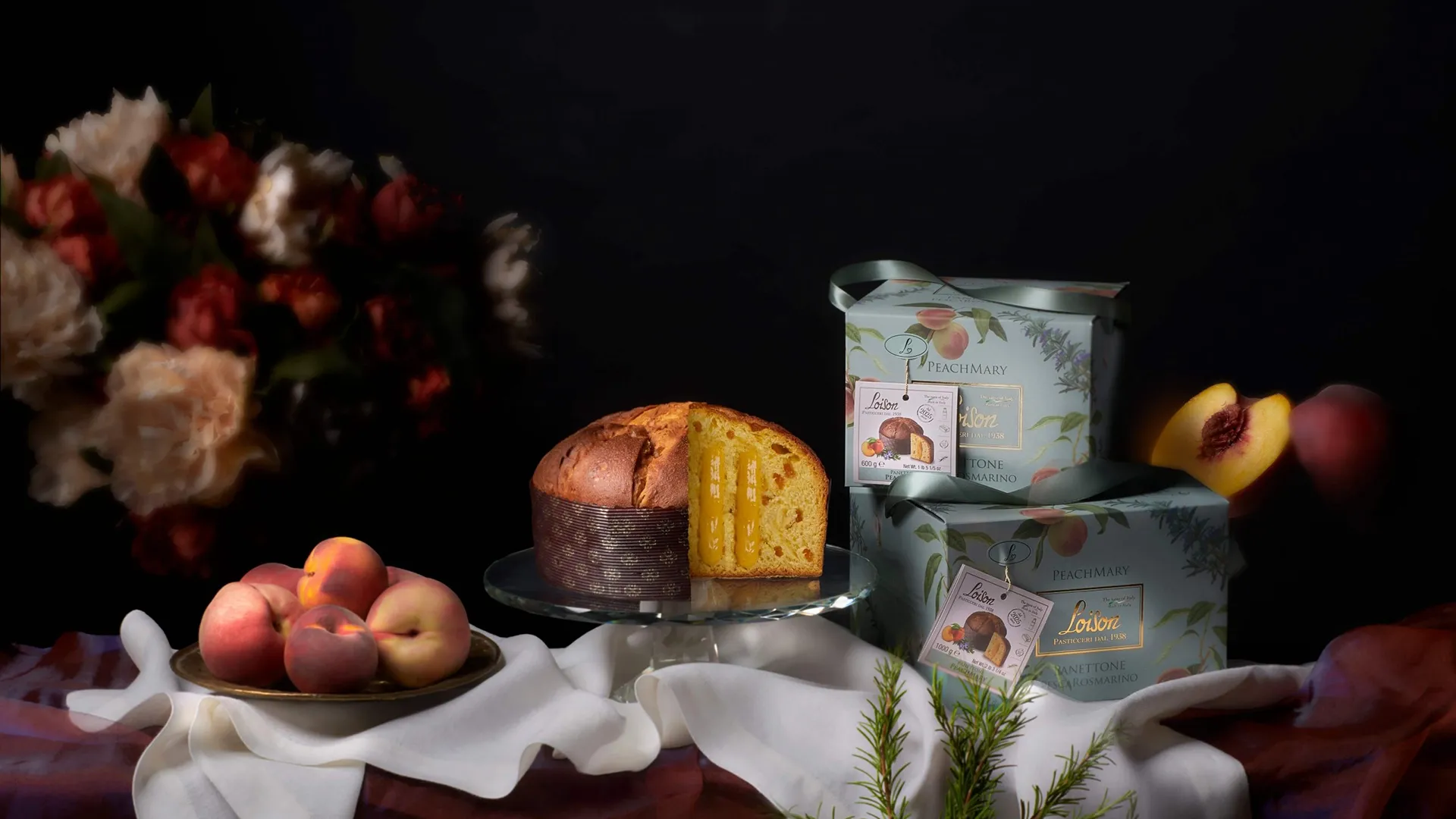 Slice of peach-filled cake on a silver stand beside pastel peach boxes and fresh peaches against a dark background.