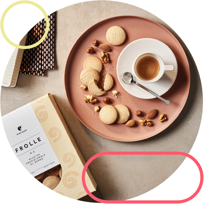 Pink plate with round cookies and almonds surrounding a white espresso cup on a saucer; cookie box on the side.