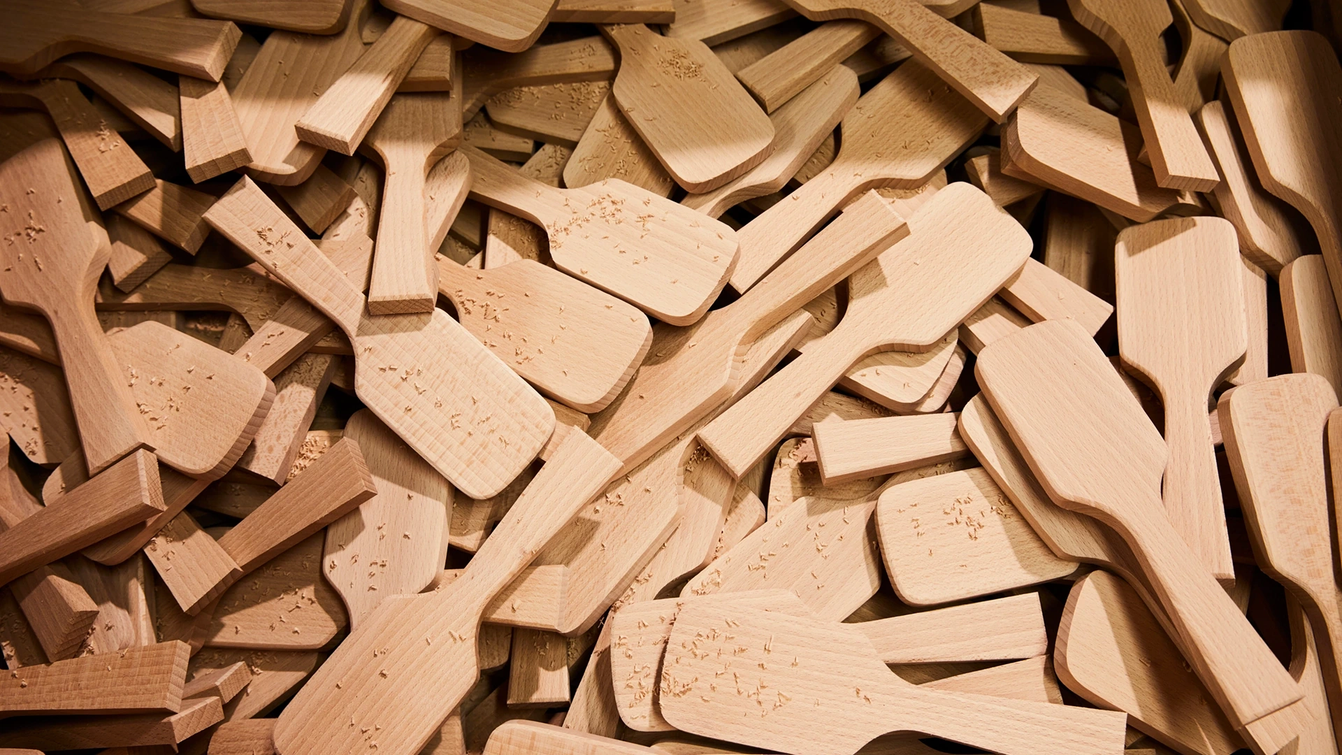 A dense pile of light wooden spatulas and paddles with rounded ends.