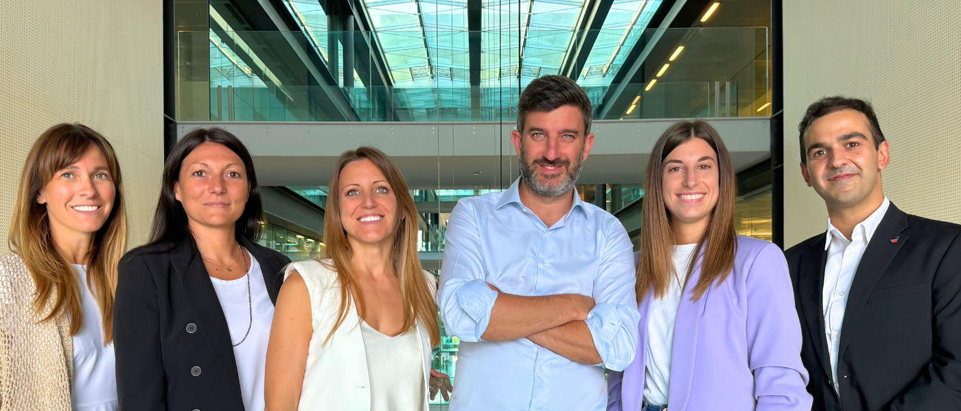 Six professionals posing for a team photo in a bright, modern office atrium, smiling at the camera.