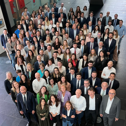Large diverse group of professionals posing for a corporate group photo in a modern office lobby.