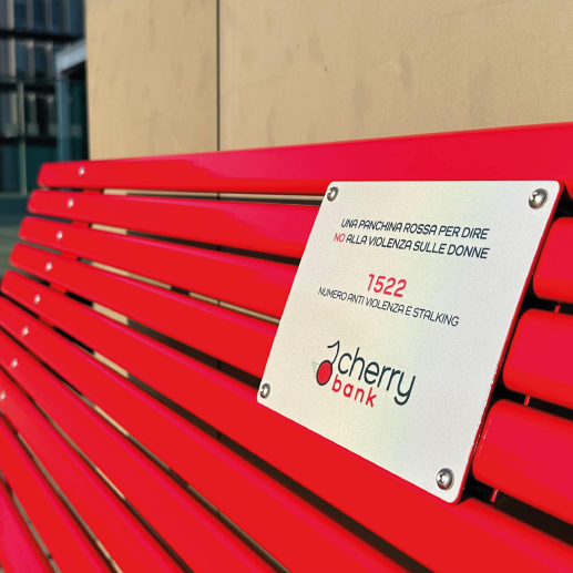 Red commemorative bench with a metal plaque promoting anti-violence against women, including the number 1522 and Cherry Bank branding