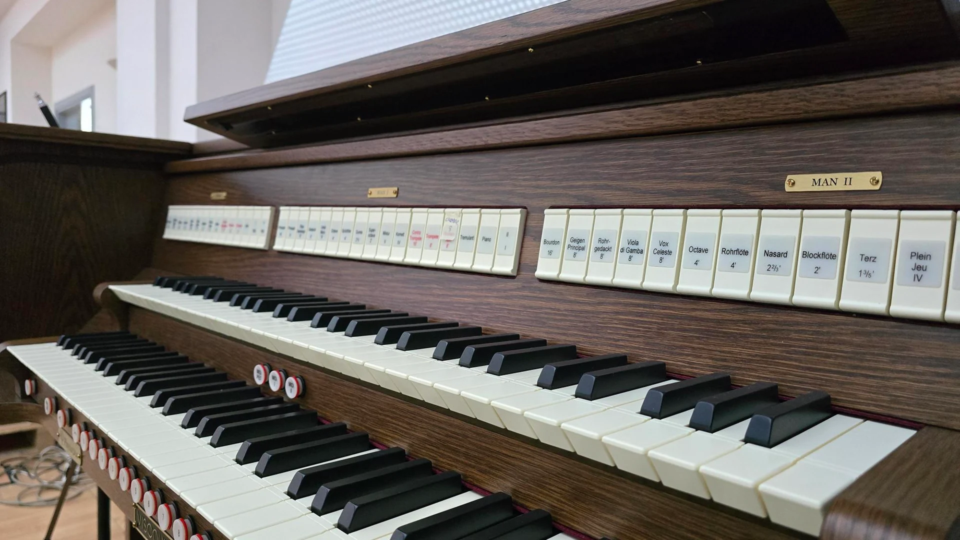 Full view of a wooden pipe organ console with two keyboards and multiple rows of stop tabs on the front panel.