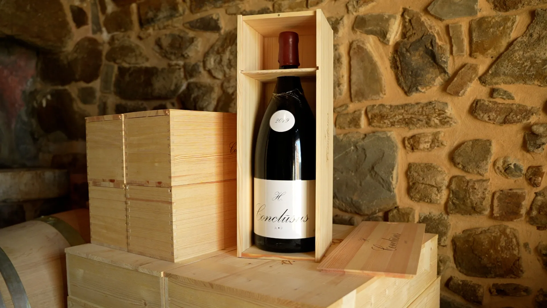 Wine bottle in a wooden crate, set on a wooden table against a stone wall in a cellar.